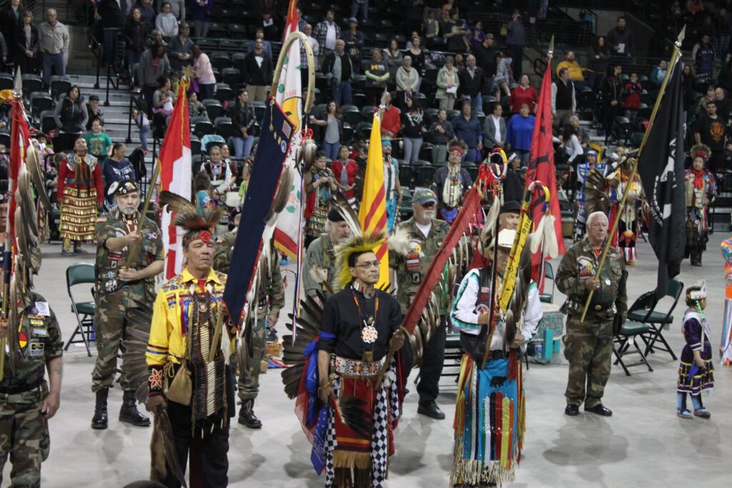 8 Indigenous people gather together and present flags and eagle staphs to be honored at a Pow Wow Grand Entry Ceremony in Minnesota.