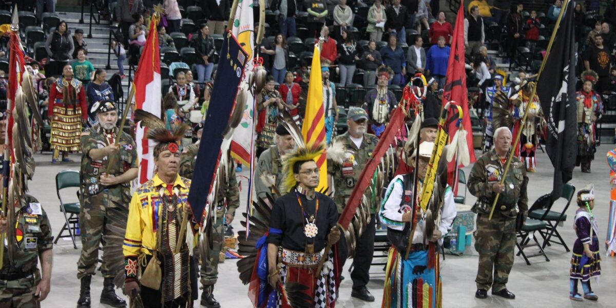 8 Indigenous people gather together and present flags and eagle staphs to be honored at a Pow Wow Grand Entry Ceremony in Minnesota.