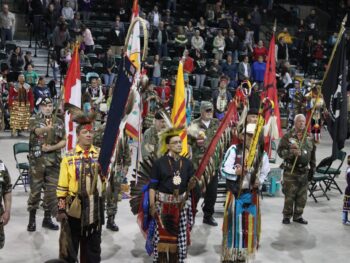 8 Indigenous people gather together and present flags and eagle staphs to be honored at a Pow Wow Grand Entry Ceremony in Minnesota.